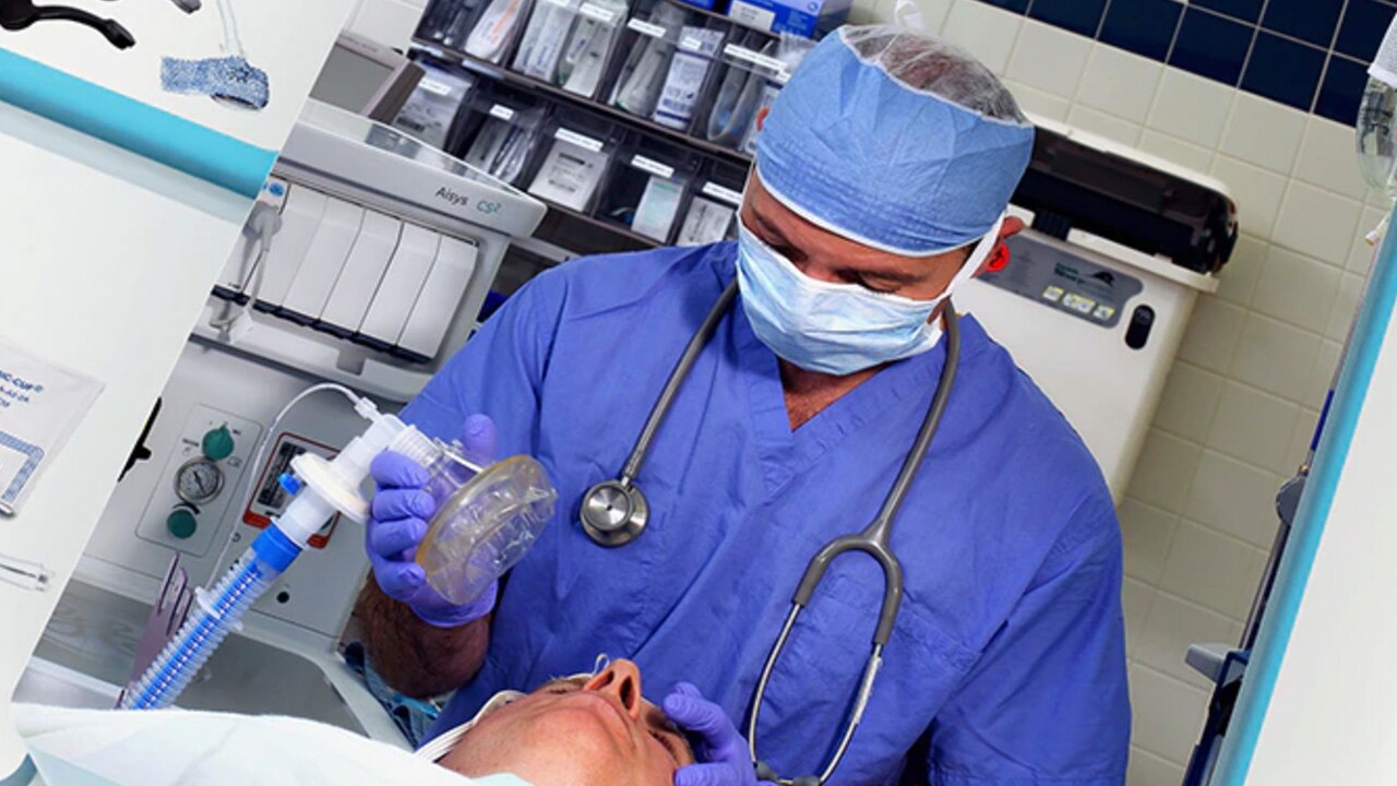 healthcare worker holidng an anesthesia mask over a patient's face